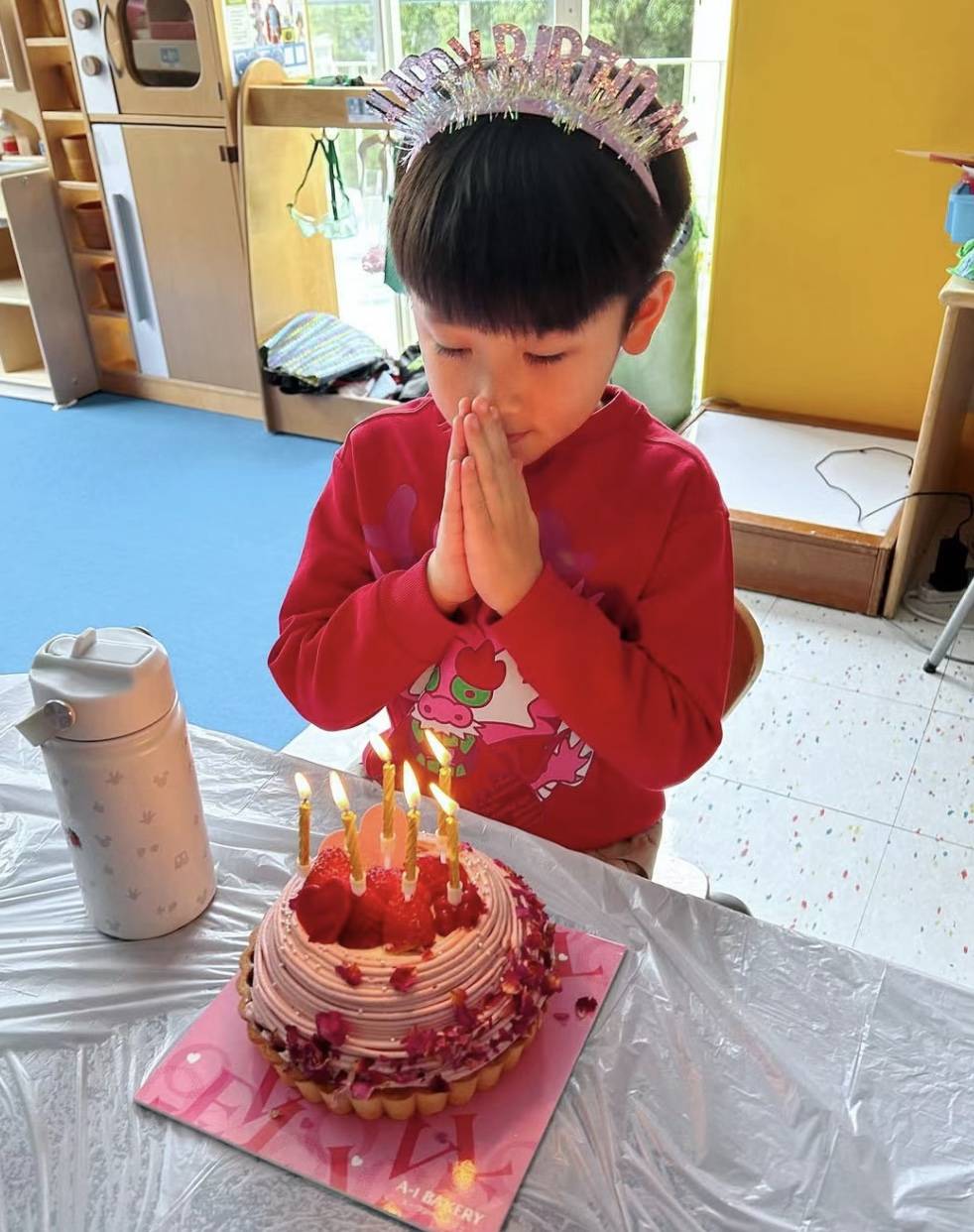 对着蛋糕小家伙不忘许愿，当天他穿着红色的上衣，头上还戴着印有生日快