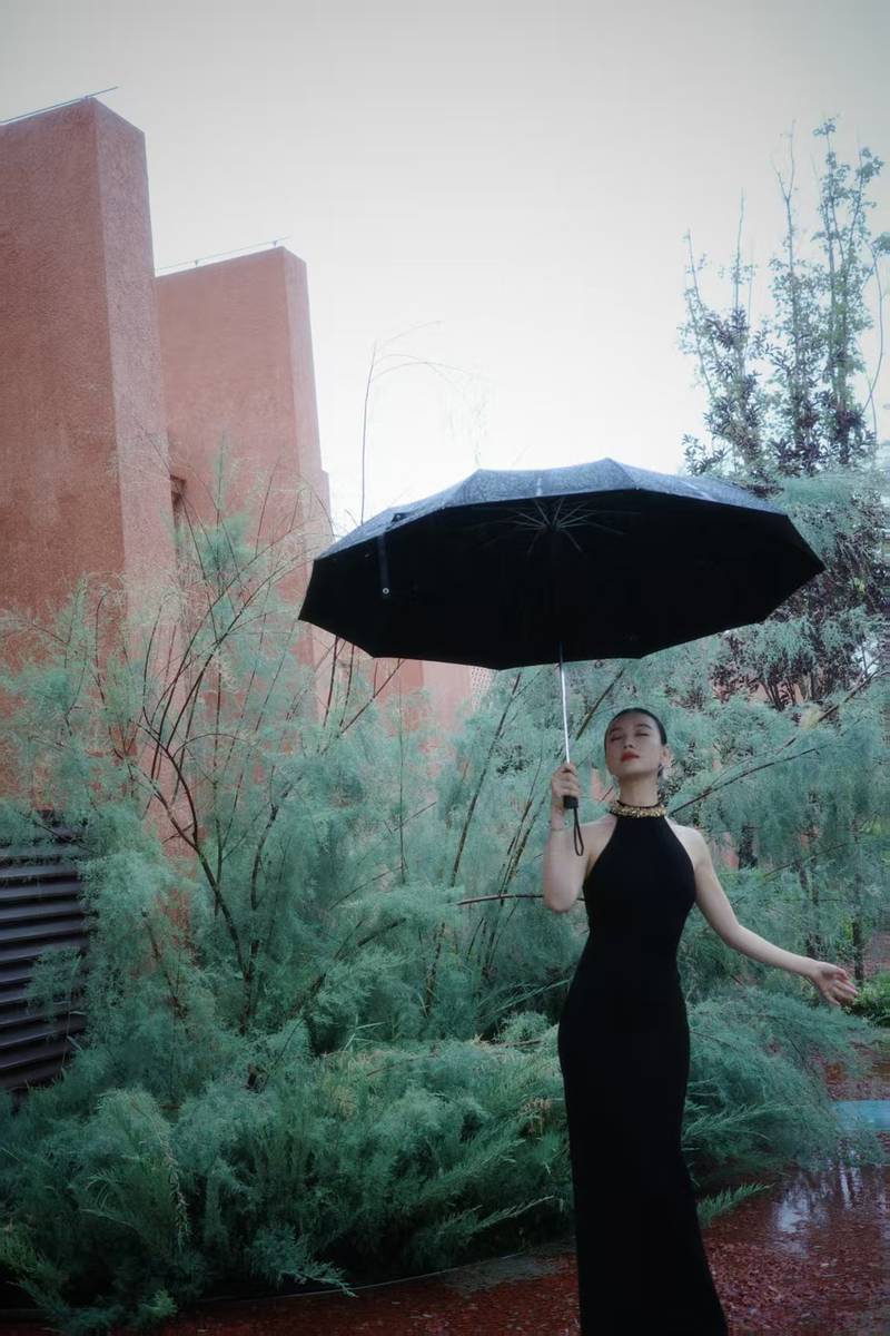 倪妮穿挂脖裙身材曼妙 撑黑伞漫步雨中尽显故事感